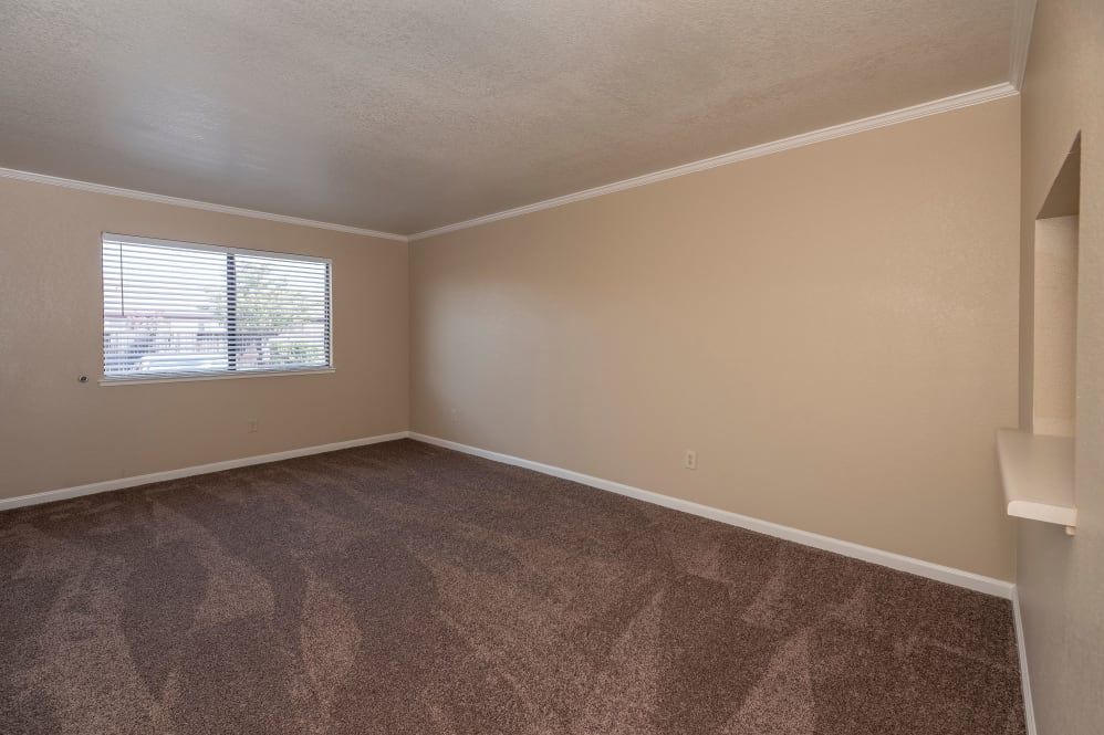 An empty room with beige walls, a window, and a carpeted floor.