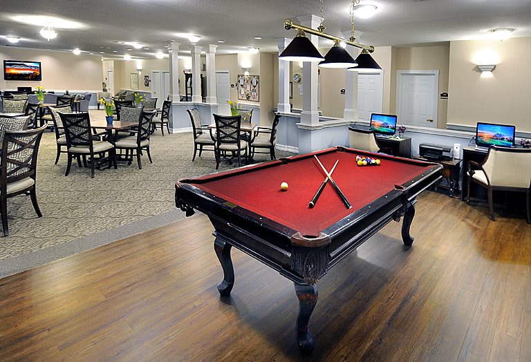 A modern recreation room featuring a pool table with red felt and surrounding seating areas.