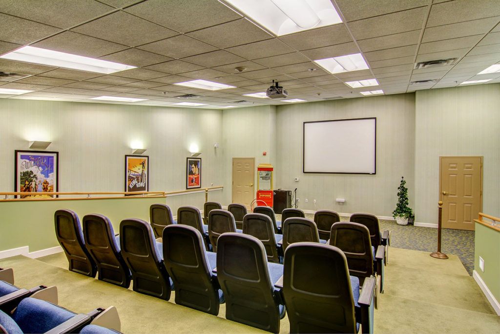 An empty conference room with rows of chairs facing a projector screen.
