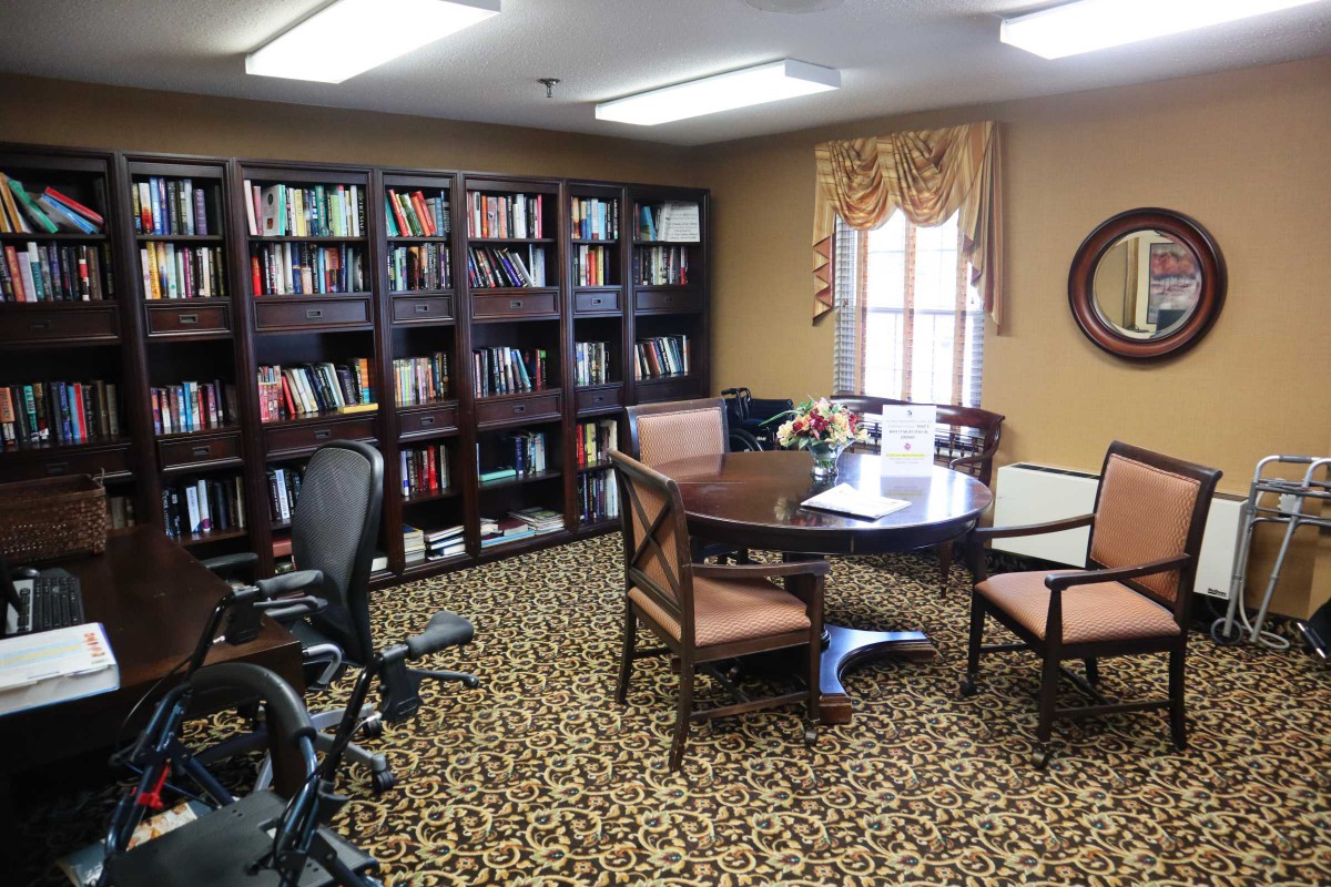 A cozy office library with bookshelves, a round table, and chairs.