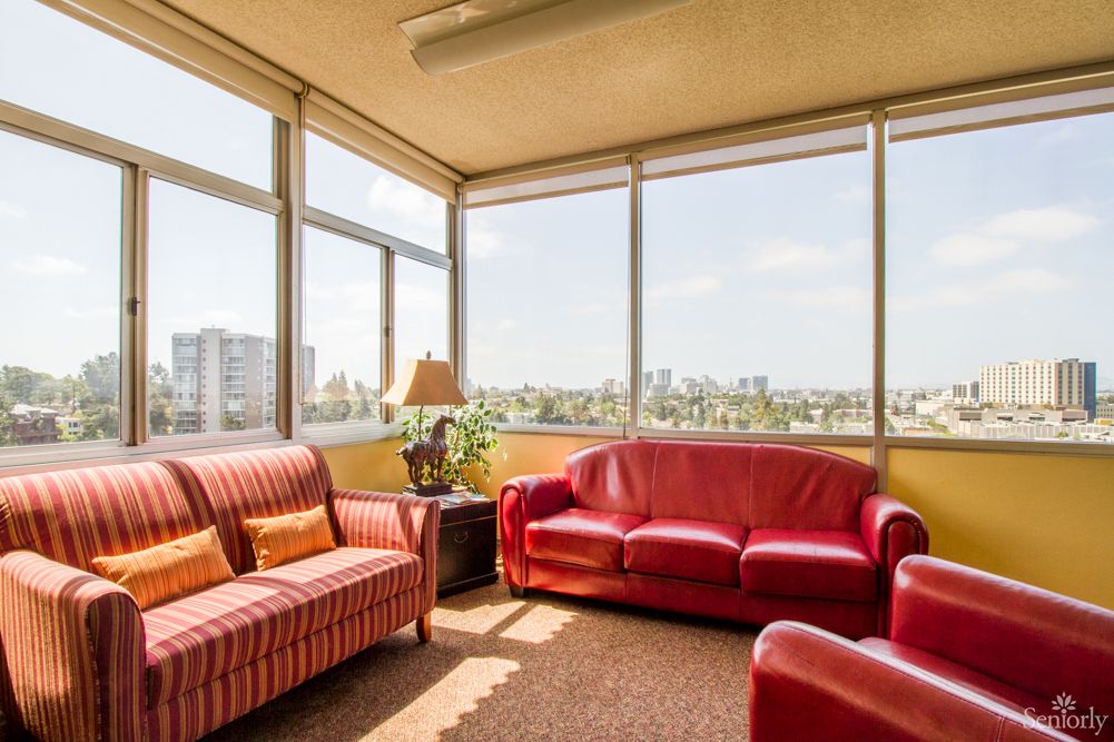 A cozy living room with red sofas and large windows offering a city view.