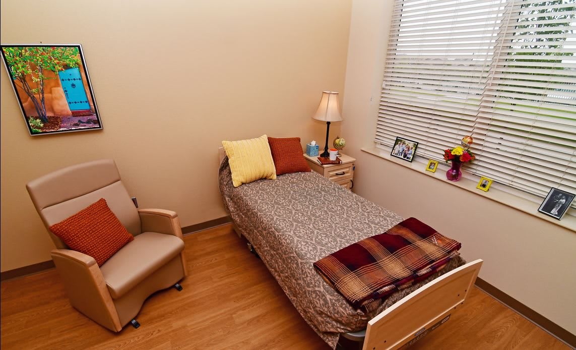 A cozy bedroom with a single bed, chair, and table lamp by the window.