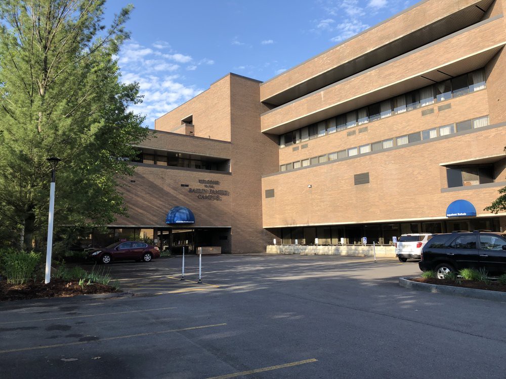 A large brick hospital building with a parking lot in front and trees surrounding it.