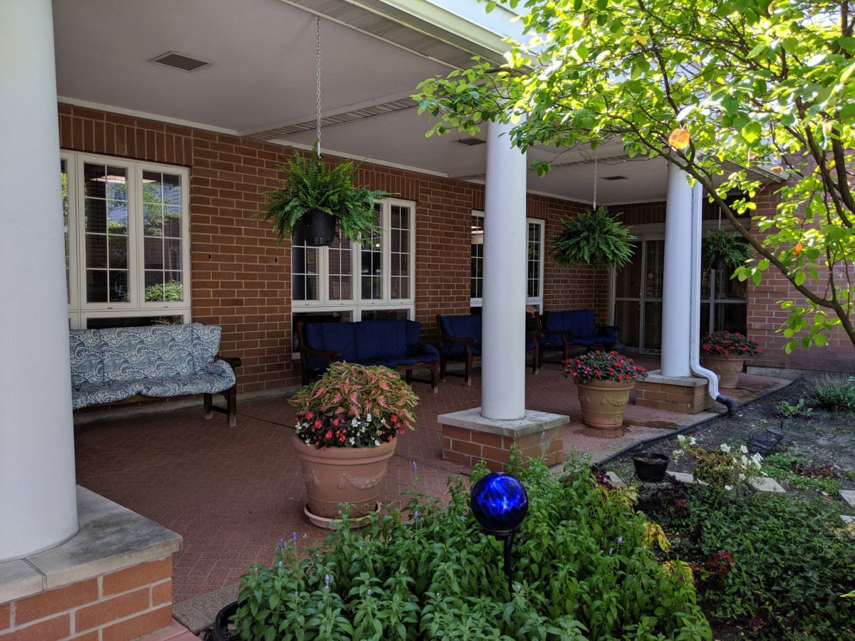 A porch with benches, potted plants, and hanging greenery under a covered area.