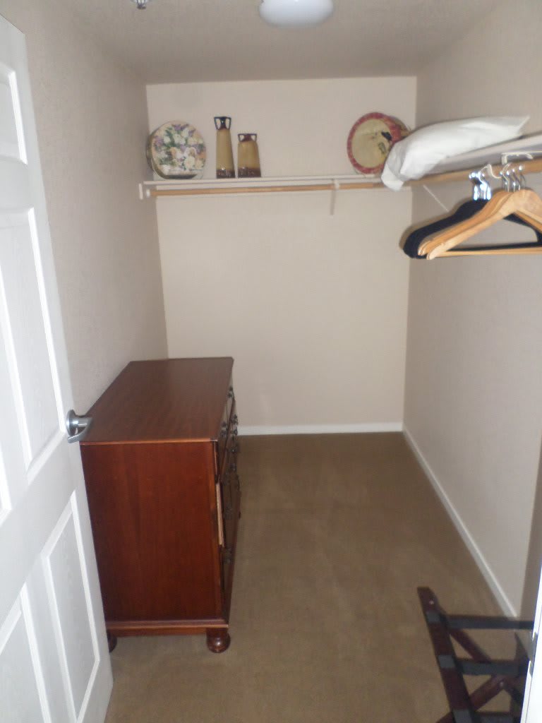 A small closet with a wooden dresser, hanging rod with hangers, and a shelf containing decorative items.