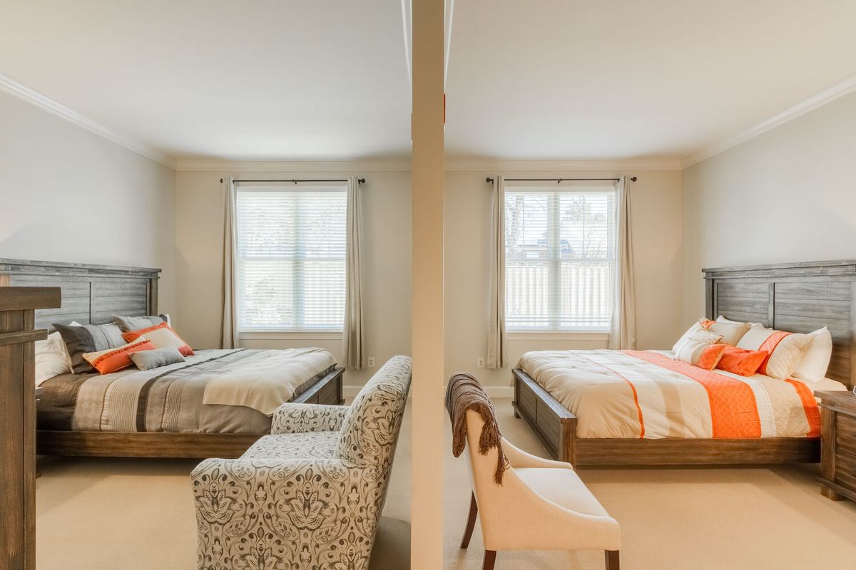 A symmetric arrangement of twin beds and chairs in a neutral-toned bedroom with large windows.