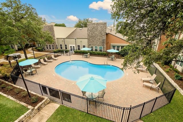 An aerial view of a residential swimming pool surrounded by patio furniture and trees.