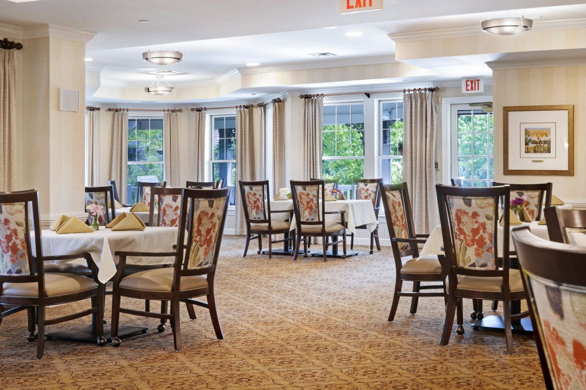 A spacious dining room with neatly arranged tables and chairs, featuring large windows and elegant curtains.