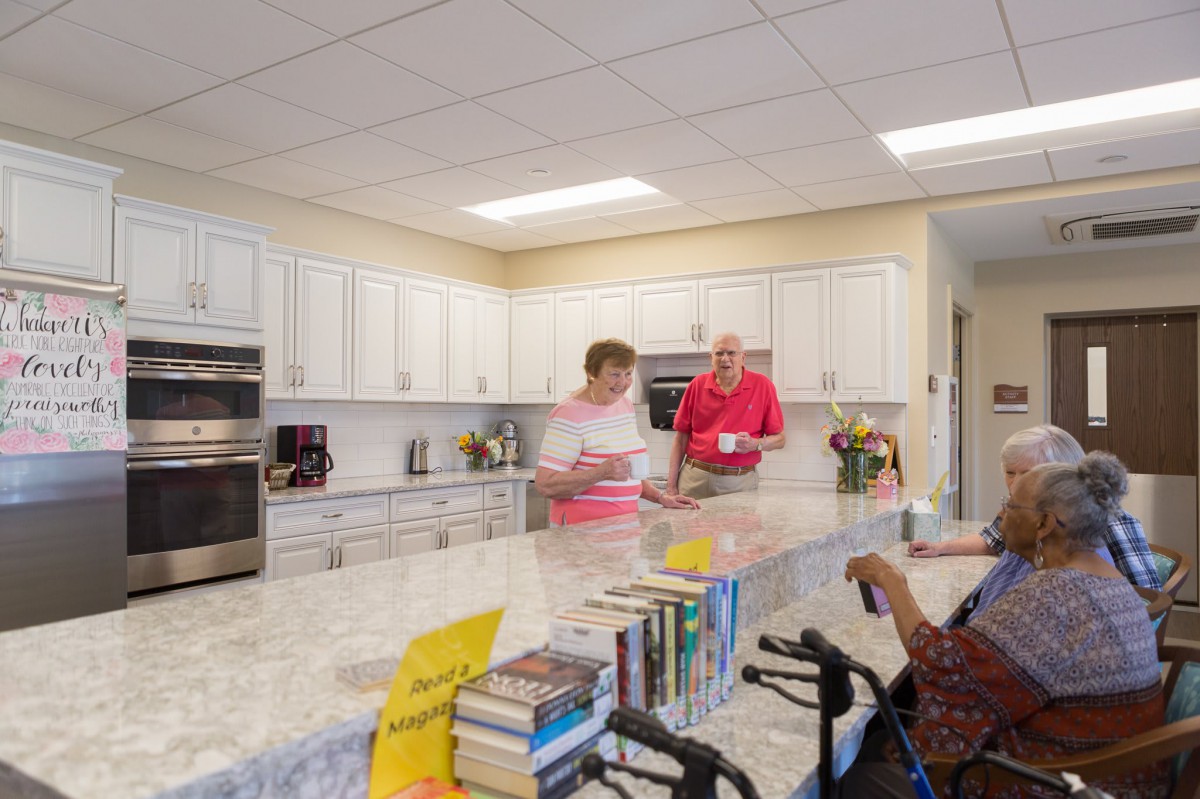 People talking in a kitchen with books on the countertop.