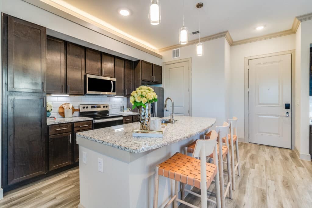 A modern kitchen with a central island featuring granite countertops and wooden bar stools, complete with stainless steel appliances and elegant pendant lighting.