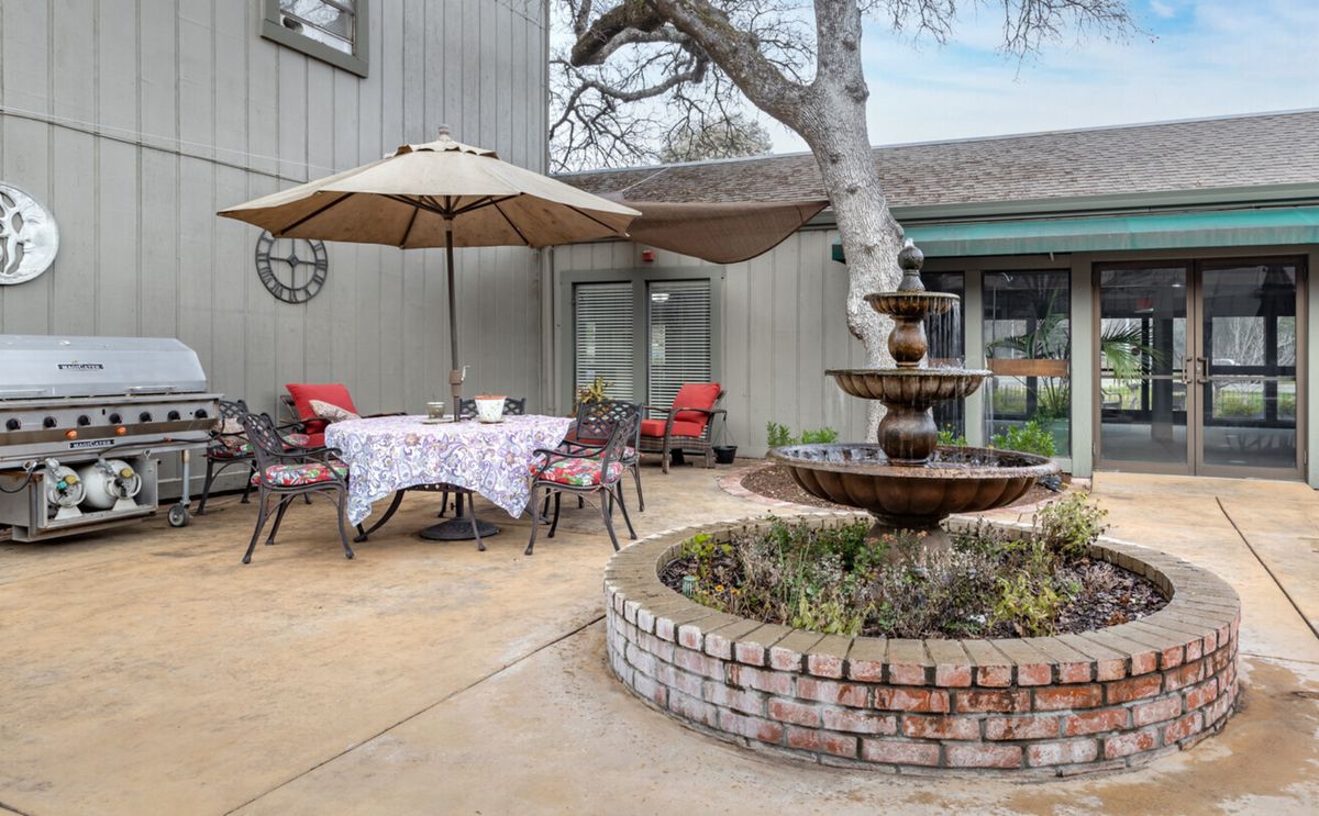 A cozy patio with a central fountain, surrounded by outdoor seating and a table under an umbrella.
