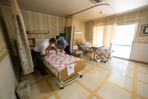 Two medical staff members preparing patient beds in a hospital room.