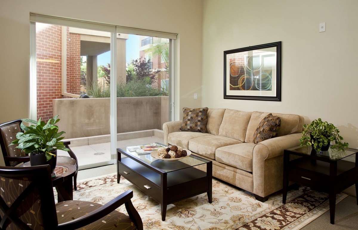 A cozy living room with a beige sofa, coffee table, and artwork, featuring a sliding glass door leading to an outdoor area.