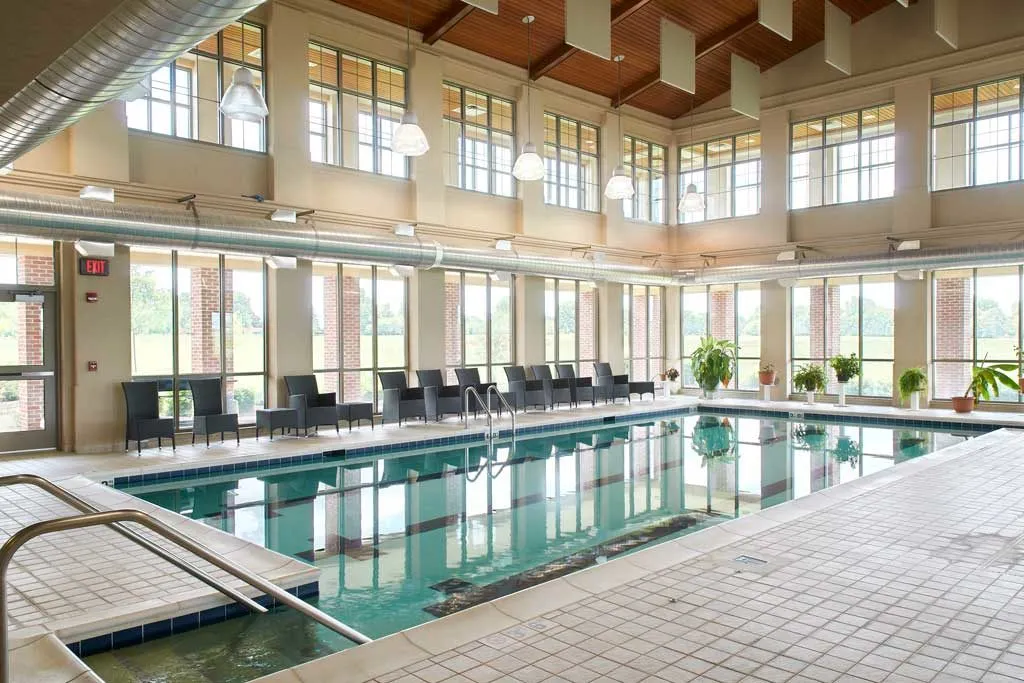 A luxurious indoor swimming pool surrounded by large windows and comfortable lounge chairs.