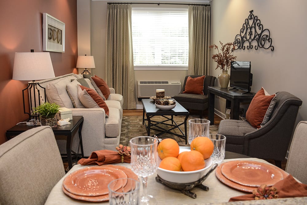 A cozy living room with warm orange accents, featuring a sofa and a dining table set with plates and glasses.