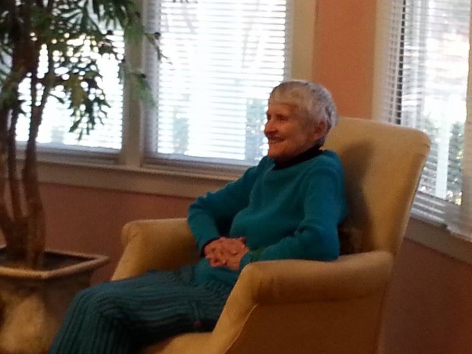 An elderly woman sitting comfortably in a chair near a window.