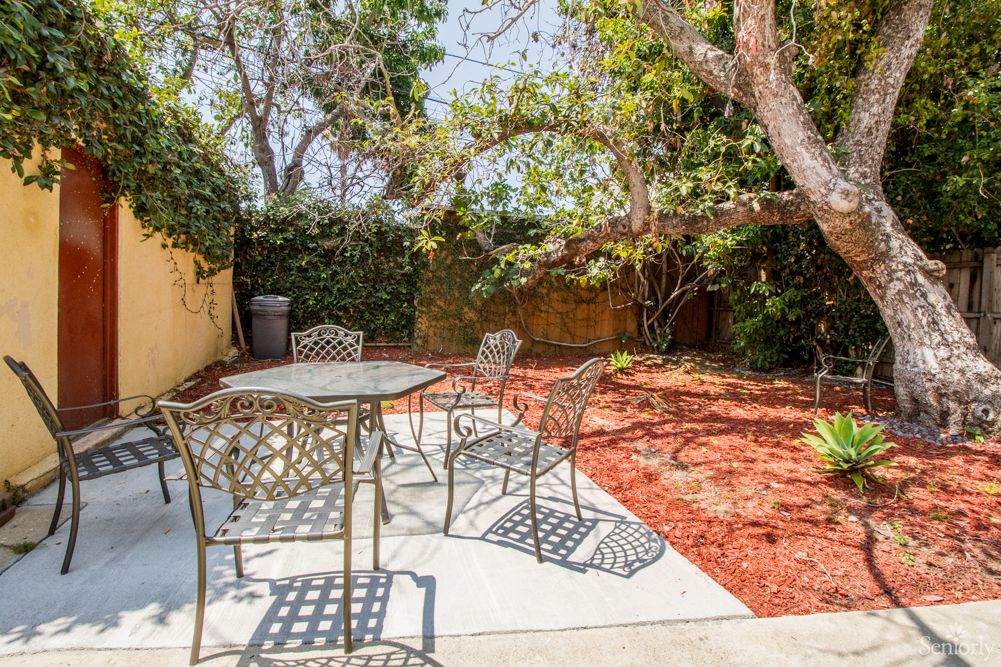 A peaceful backyard patio with metal furniture, surrounded by lush trees and garden space.