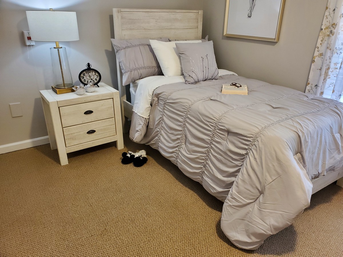 A cozy bedroom with a neatly made bed and a bedside table featuring a lamp and clock.