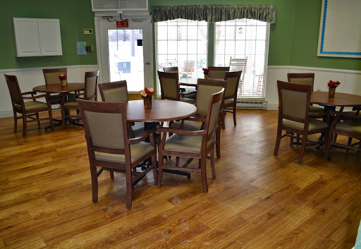A cozy dining area featuring wooden tables and chairs, surrounded by green walls and large windows.