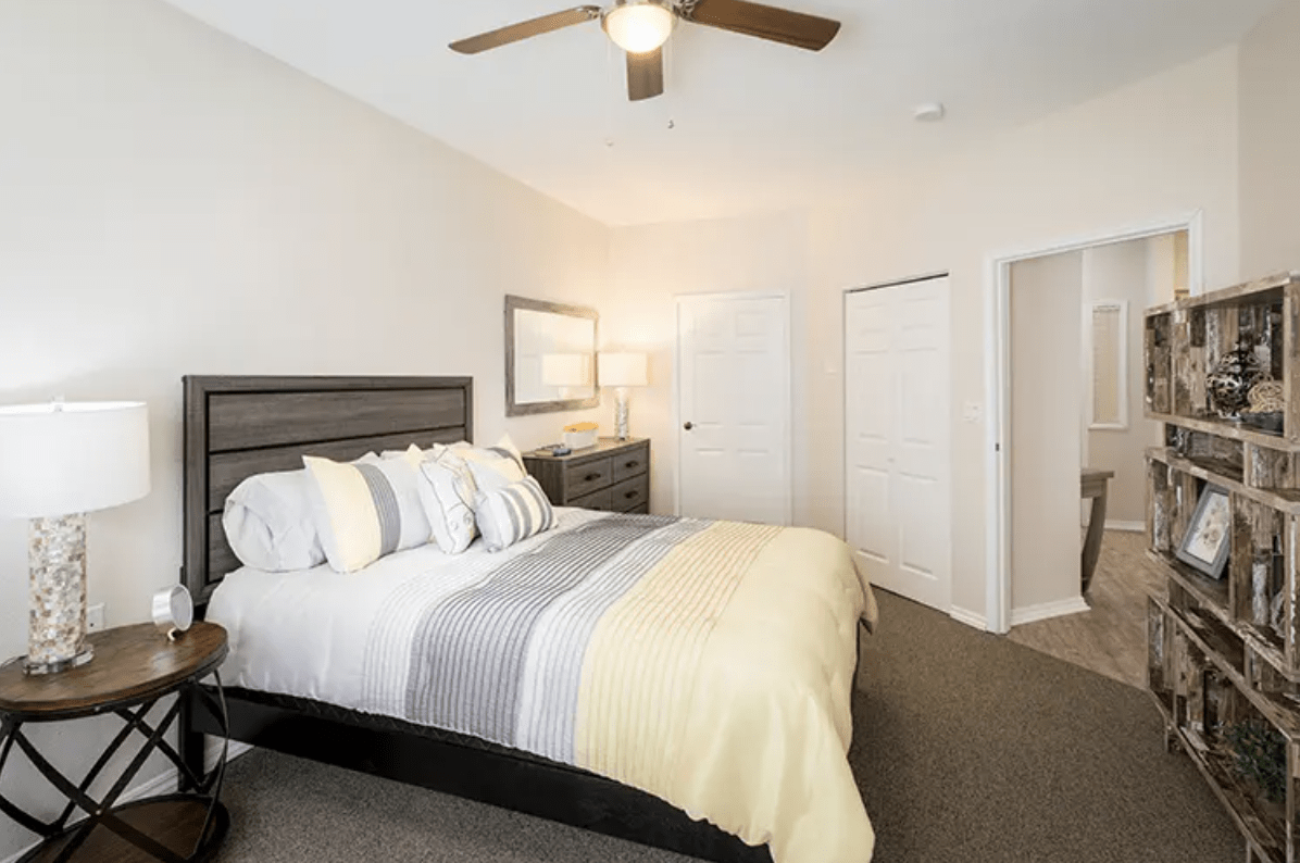 A modern bedroom with a neatly made bed, ceiling fan, and minimalist decor.