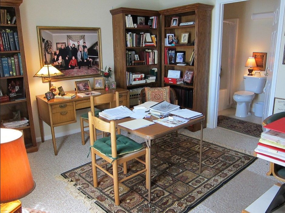 A home office with a desk covered in papers, surrounded by bookshelves and decorations.