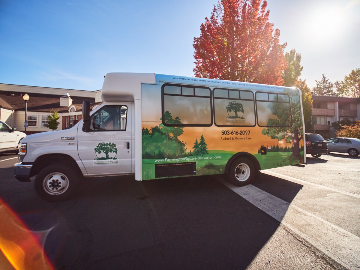 A shuttle bus with a nature-themed design parked under the autumn sun.