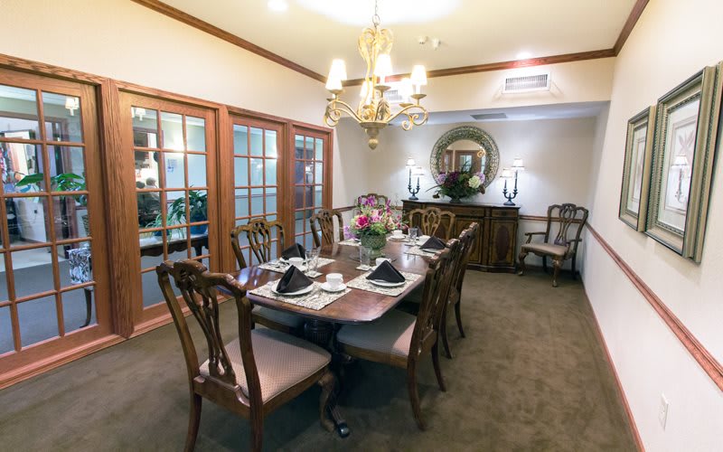 An elegant dining room setup featuring a long table with chairs, adorned with a chandelier and decorative elements.