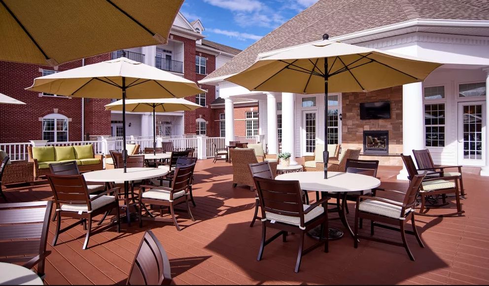A sunny outdoor patio area with tables, chairs, and large umbrellas near a brick building.