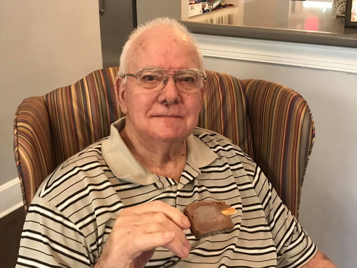 An elderly man enjoying an ice cream while sitting in an armchair.