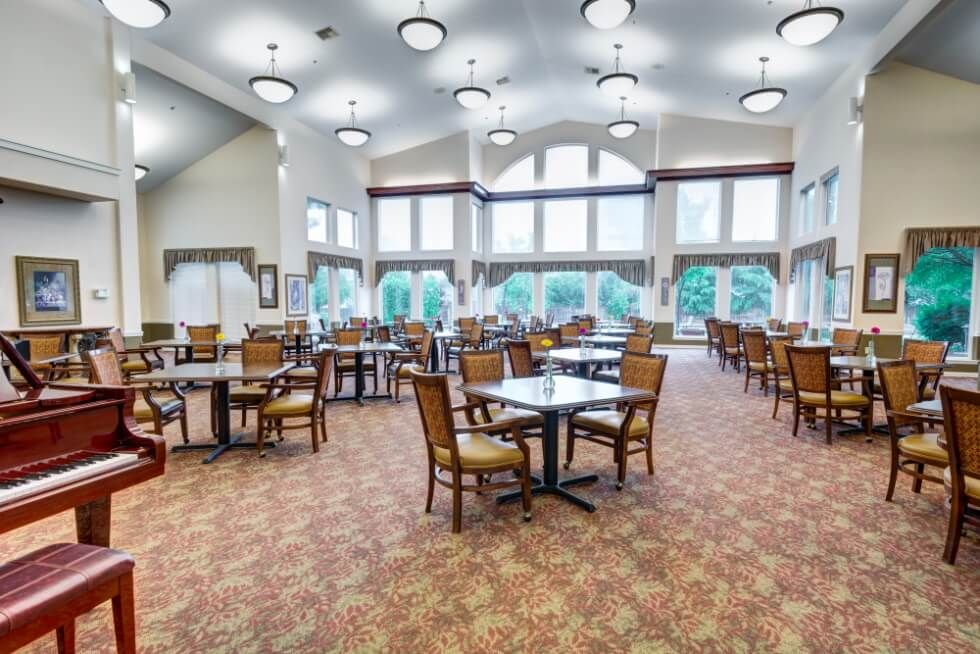 A spacious dining area with multiple tables and chairs, featuring large windows and elegant chandeliers.