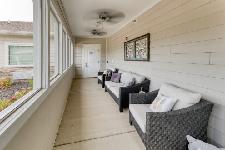 A cozy sunroom with rattan furniture and ceiling fan overlooking the outside through large windows.