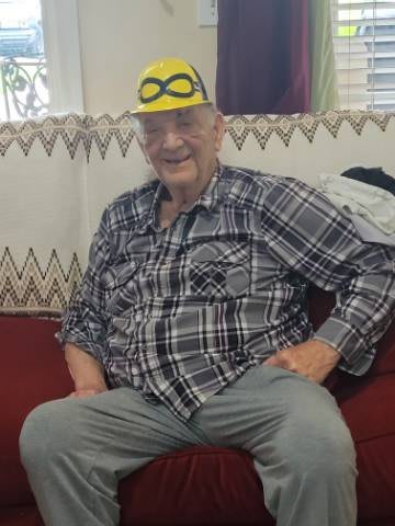 A person wearing a plaid shirt and hat, sitting on a couch and smiling indoors.