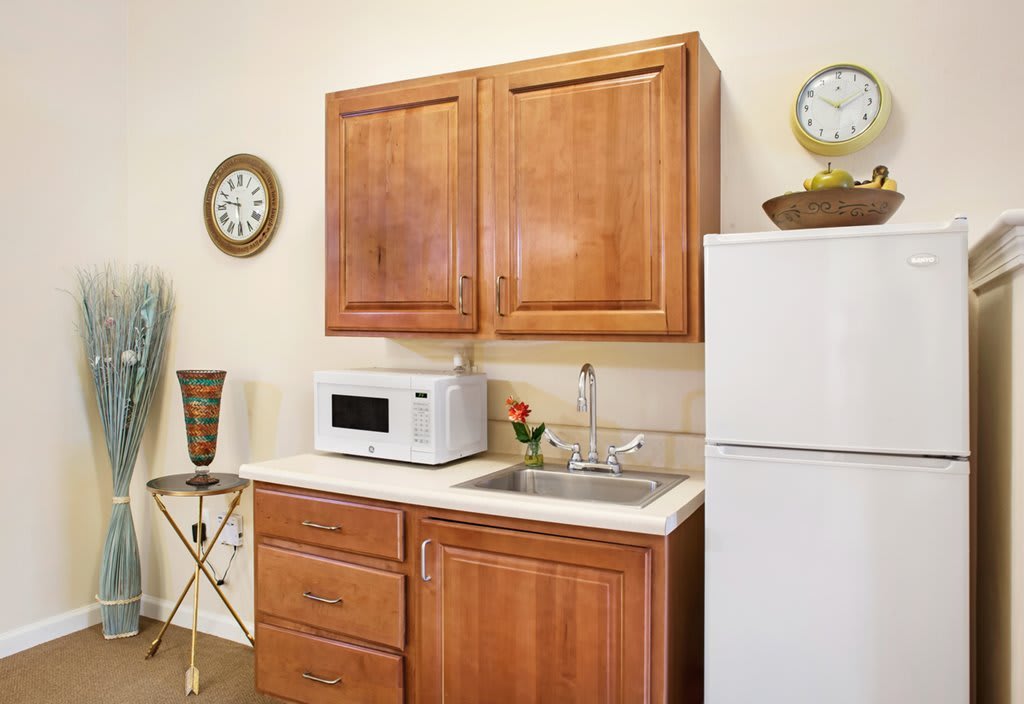 A compact kitchen setup featuring wooden cabinets, a microwave, sink, and refrigerator.