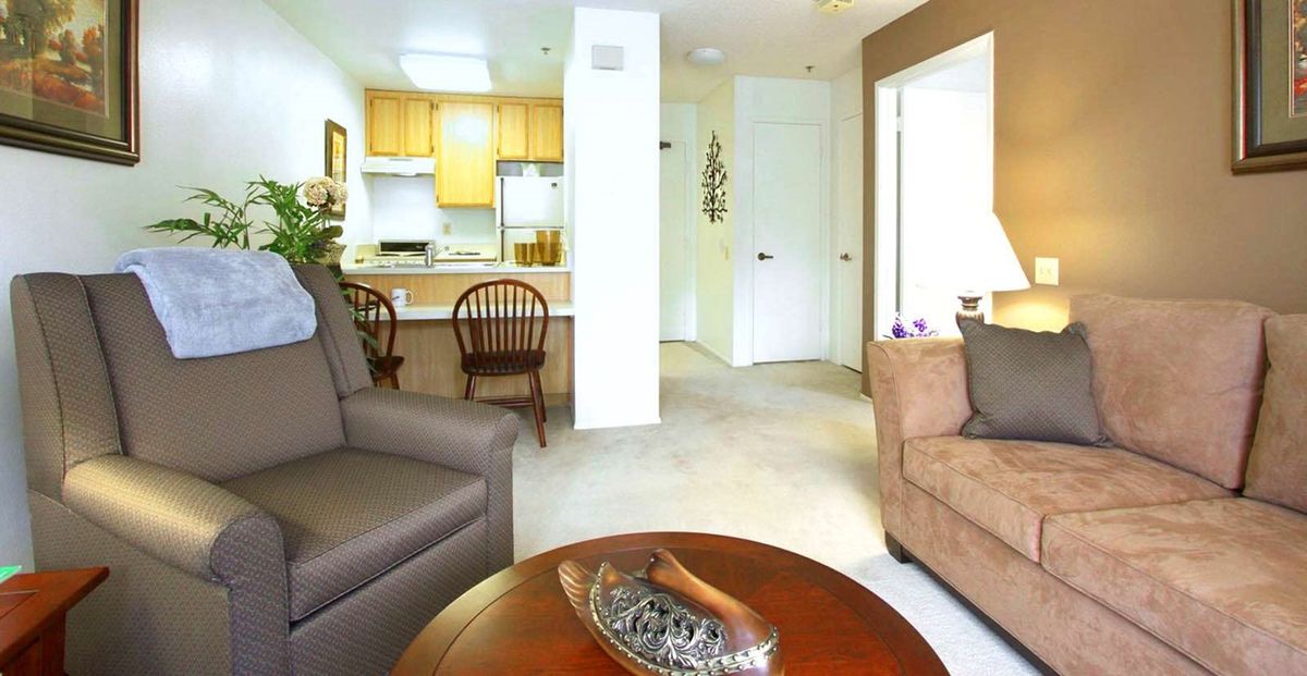 A cozy living room with a view into the kitchen area, featuring comfortable seating and a wooden table.