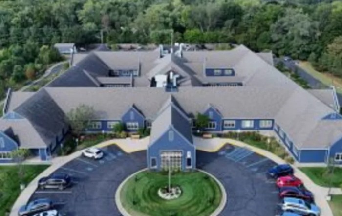 Aerial view of a large building surrounded by a parking lot and greenery.