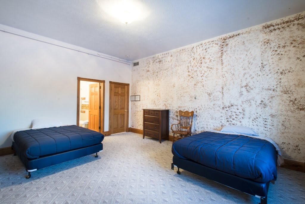 A spacious bedroom with two blue-covered beds and vintage furniture.