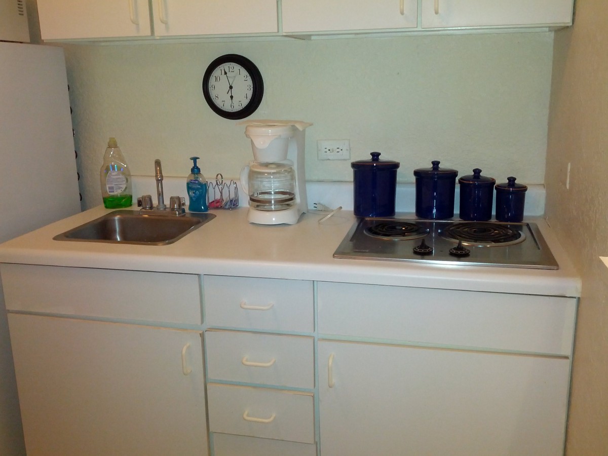 A small kitchen counter with a sink, coffee maker, and blue pots on a stove.