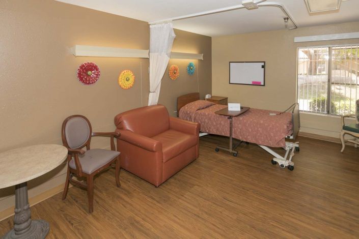 A cozy hospital room with a patient bed, chairs, and colorful wall art.