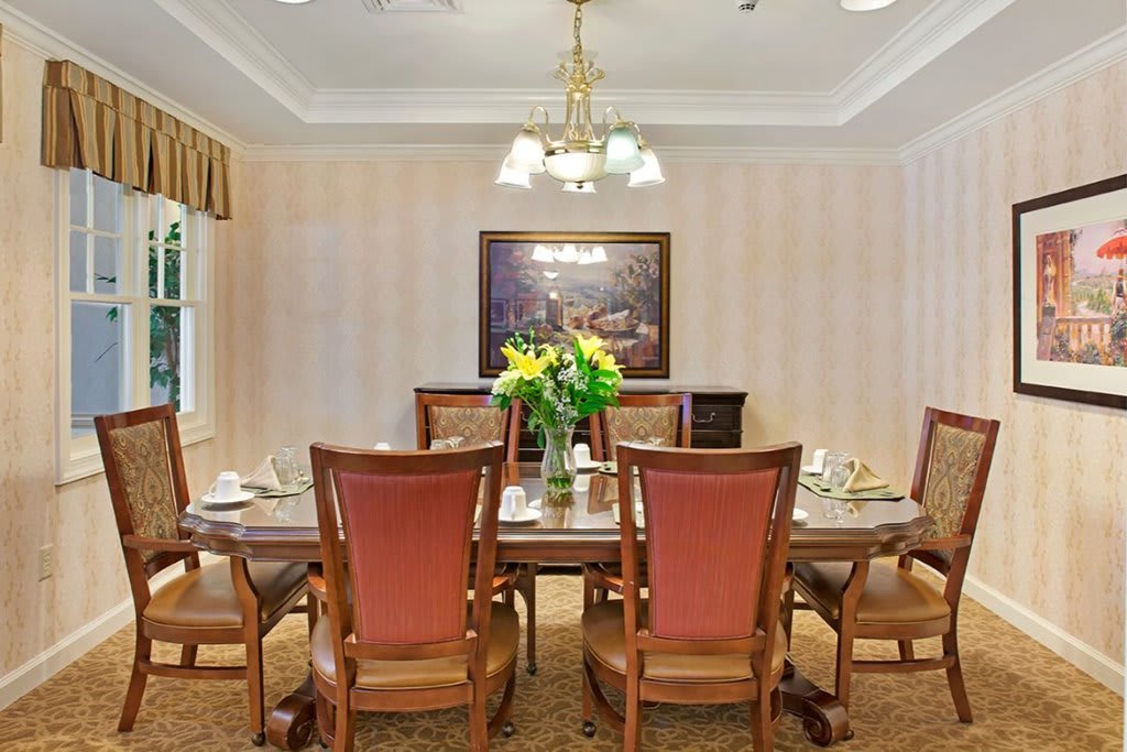A warmly lit dining room with a wooden table, surrounded by chairs and decorated with a floral centerpiece.