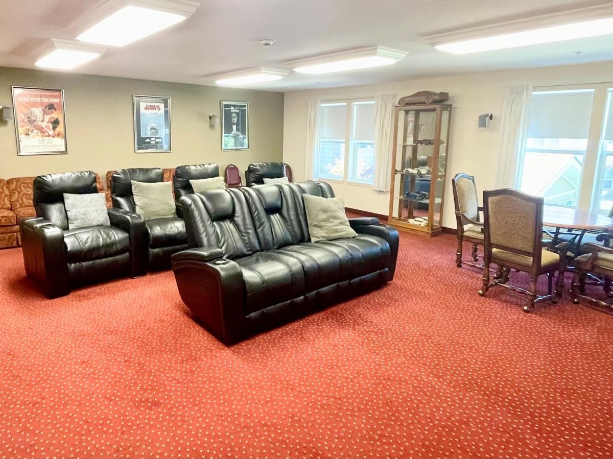 A spacious living room featuring black leather sofas, a red carpet, and a glass cabinet.