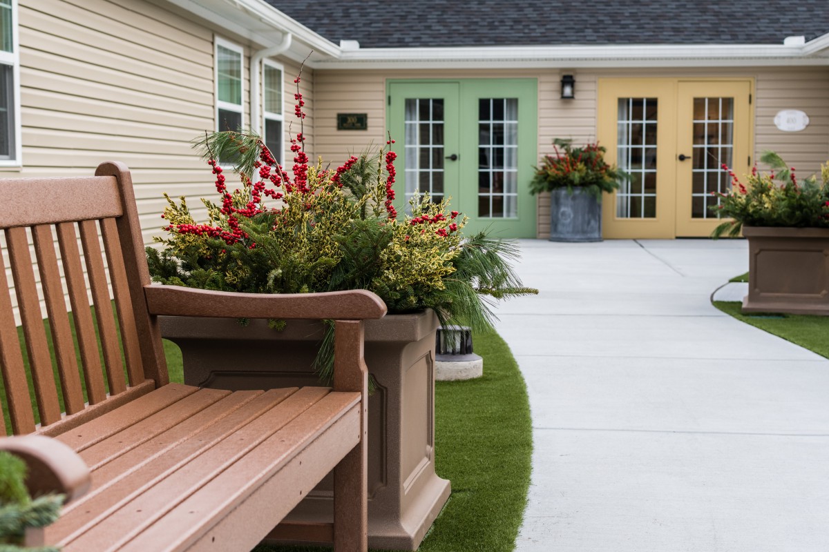A cozy patio with a wooden bench, vibrant plants, and colorful doors.