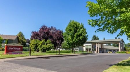 A sunny day with vibrant trees lining a quiet street next to a building.