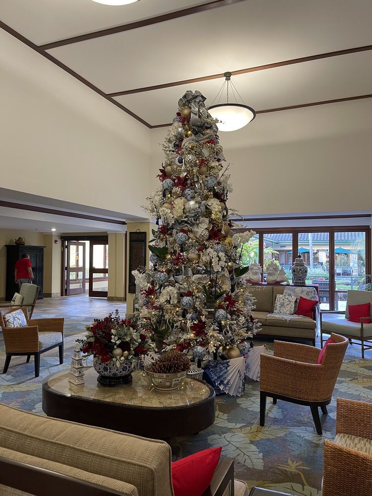 A beautifully decorated Christmas tree stands tall in a spacious lobby with comfortable seating and festive decorations.