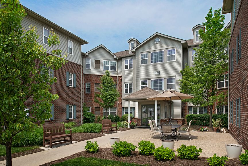 A residential building with a landscaped garden and patio area, featuring outdoor furniture and greenery.