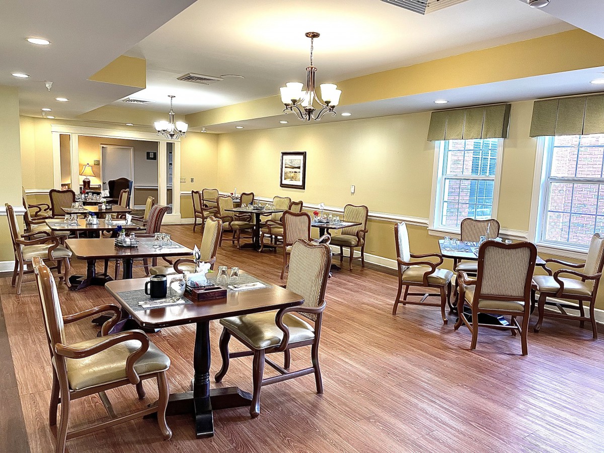 A spacious dining room with neatly arranged tables and chairs, featuring a warm wooden floor and ample lighting.