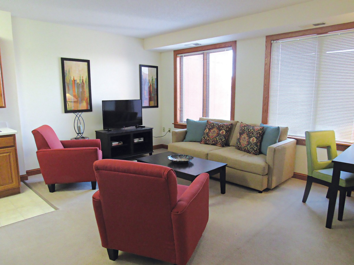 A cozy living room featuring a sofa, two red armchairs, a coffee table, and a television.
