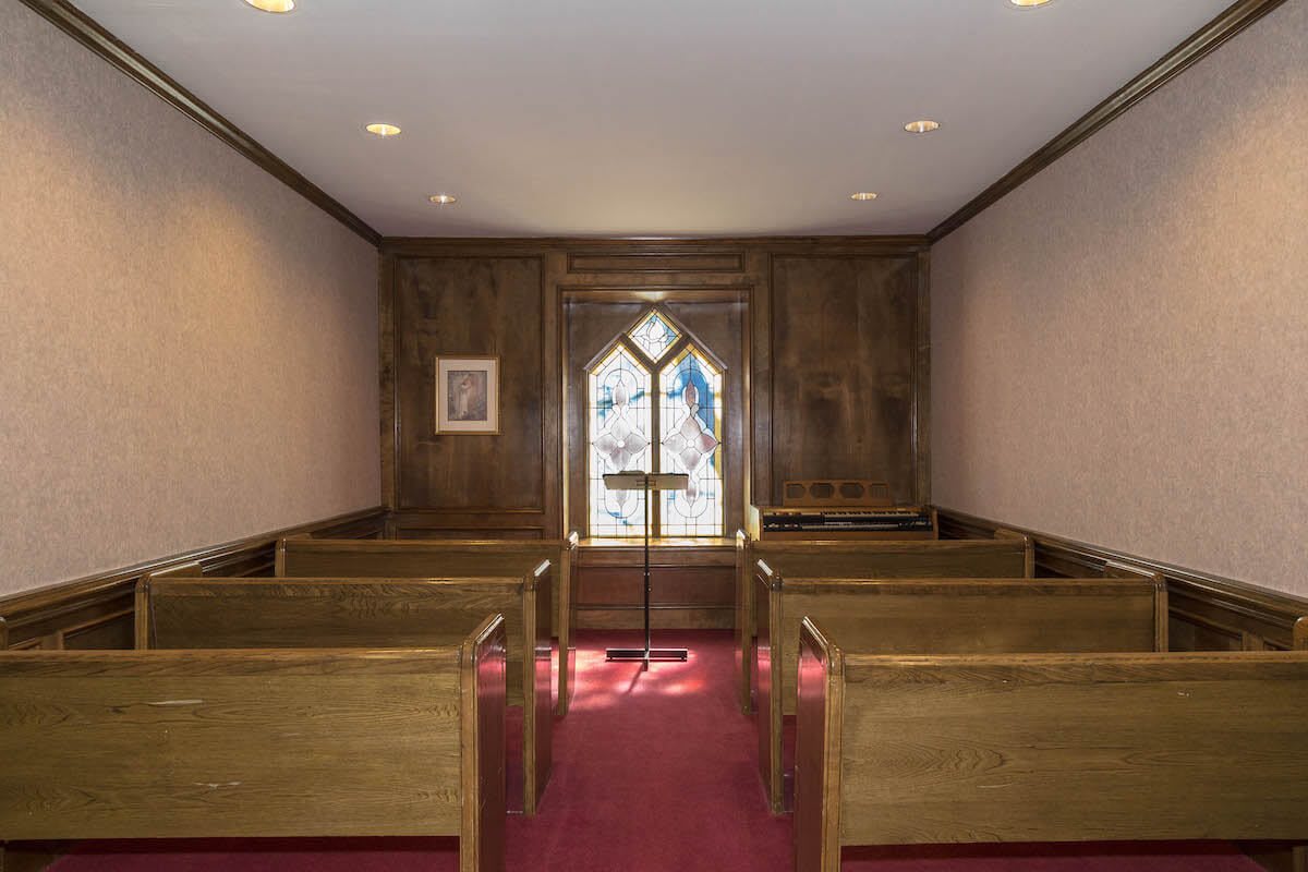 A small chapel interior featuring wooden pews and a stained glass window.