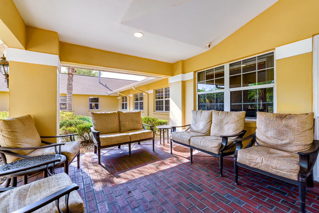 A cozy outdoor seating area on a covered patio with yellow walls and brick flooring.