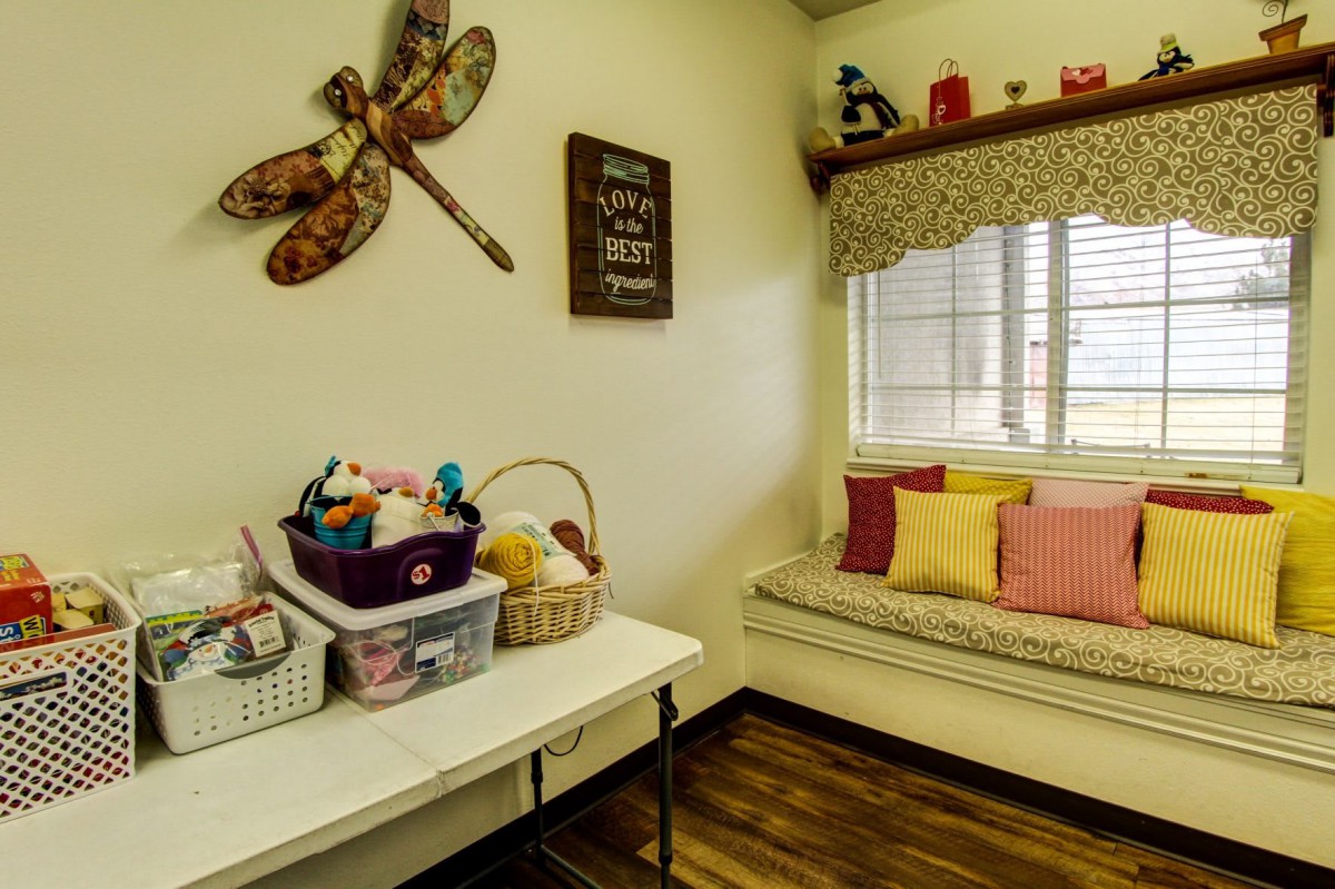 A cozy craft room with a bench, colorful cushions, and a table filled with craft supplies.