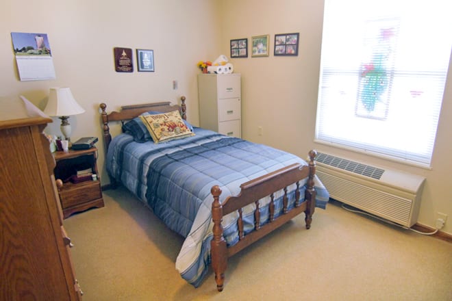 A cozy bedroom featuring a single wooden bed with blue bedding, decorated with wall art and a carpeted floor.